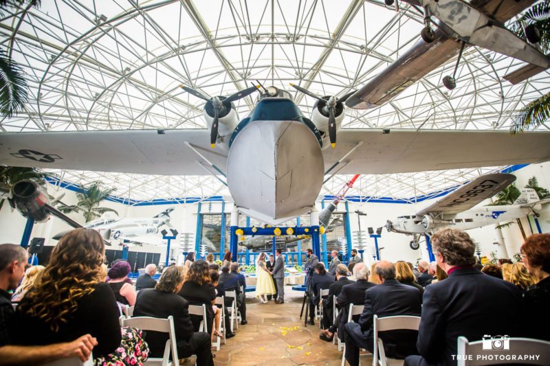 Bride and Groom hold hands under big airplane during Star Wars themed wedding ceremony at museum